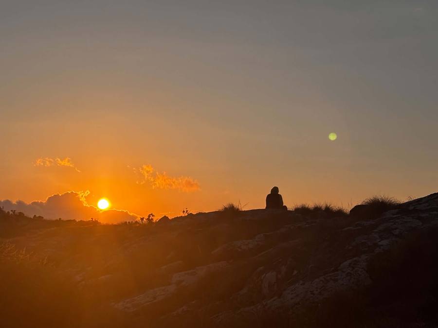 Edgison sits on a rocky plateau watching the sun set over the plain far below.